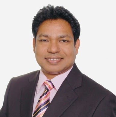 Man in suit with pink shirt, smiling.