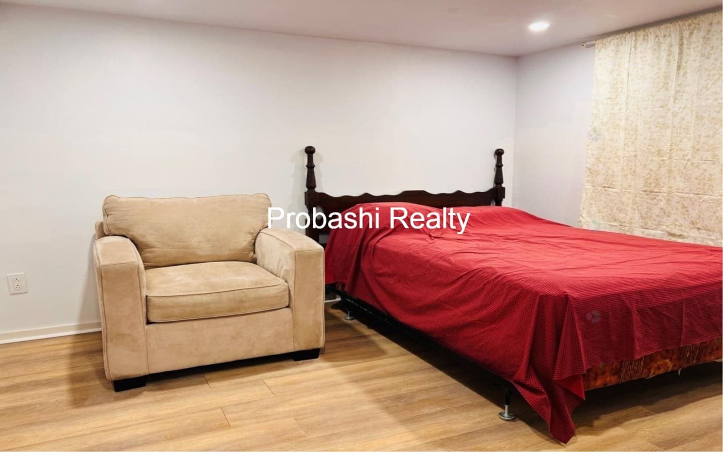 Cozy bedroom with a red bedspread and beige armchair.