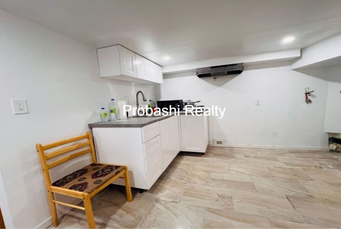 Small, modern kitchen with white cabinets and wooden chair.