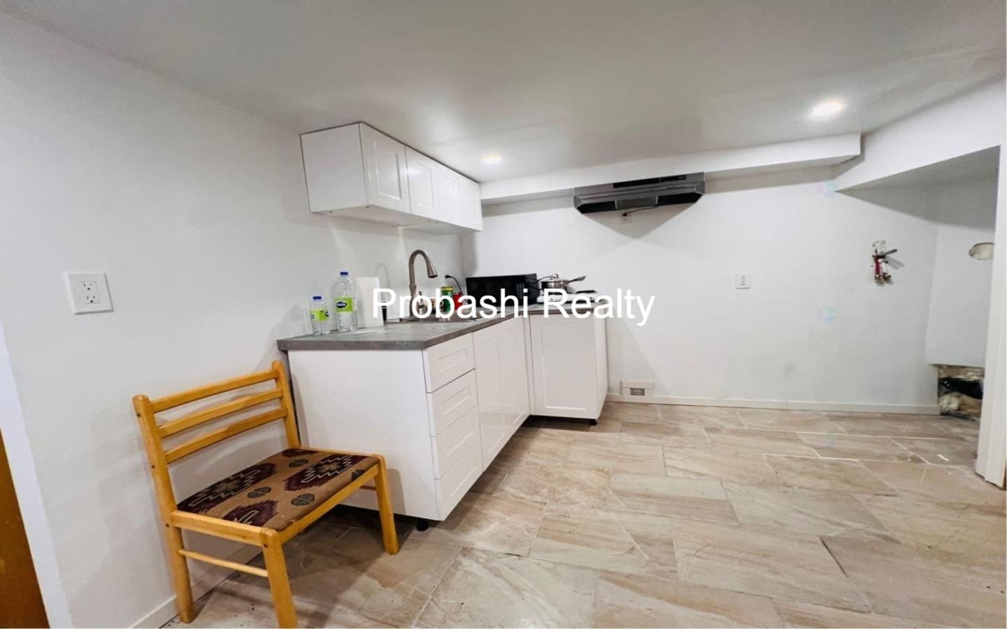 Small, modern kitchen with white cabinets and wooden chair.