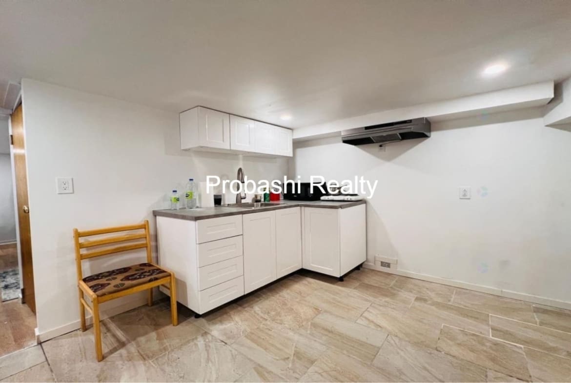 Small modern kitchenette with white cabinets and wooden chairs.